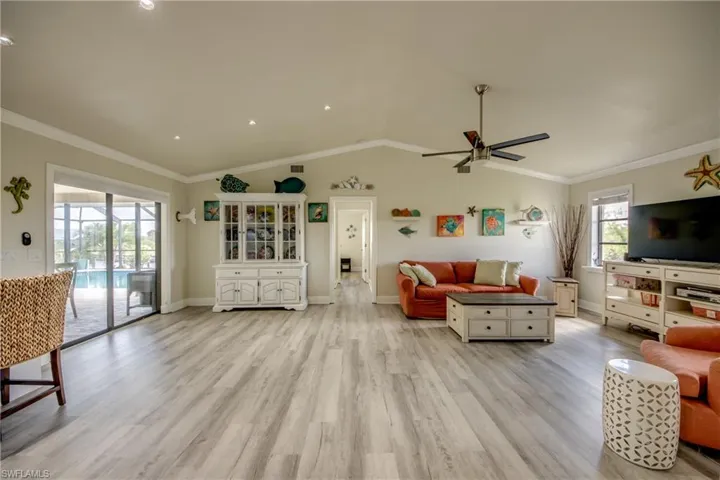 Living room with baseboards, vaulted ceiling, crown molding, ceiling fan, and light wood finished floors