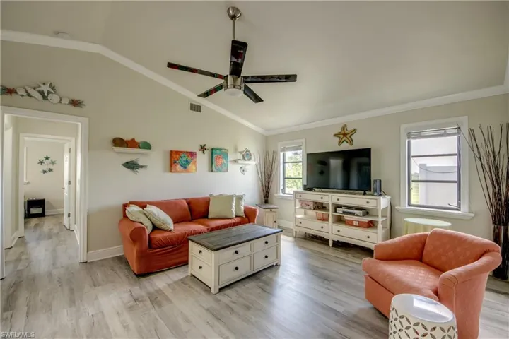 Living area featuring light wood-style floors, ornamental molding, a ceiling fan, and vaulted ceiling