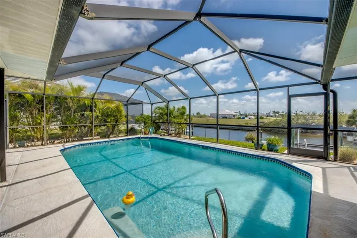 Outdoor pool with a water view, glass enclosure, and a patio