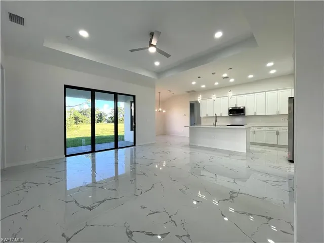 Unfurnished living room with a tray ceiling, recessed lighting, light marble finish flooring, a chandelier, and a ceiling fan