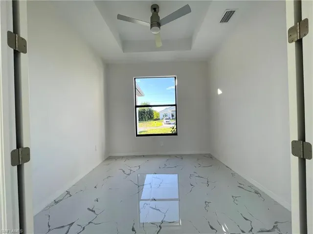 Unfurnished room featuring a raised ceiling, light marble finish floors, and ceiling fan