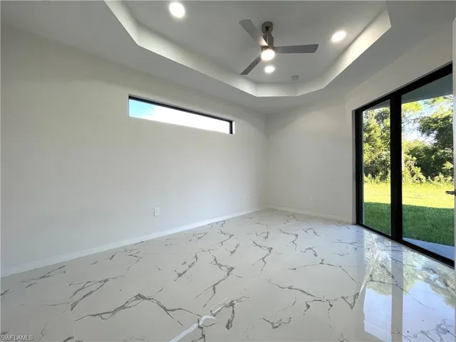 Spare room with a tray ceiling, light marble finish floors, ceiling fan, and recessed lighting