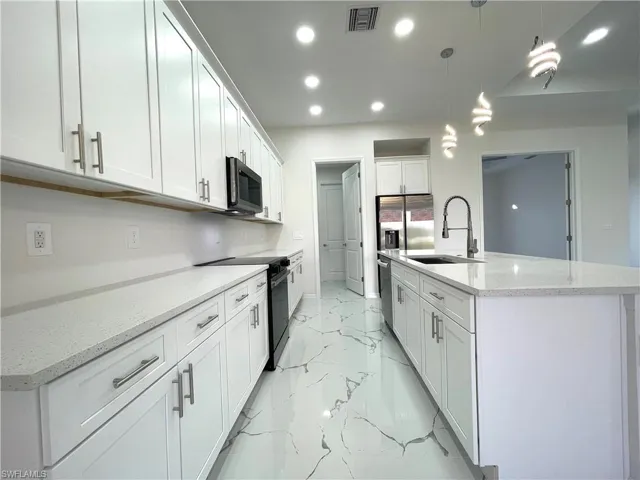 Kitchen featuring light stone counters, appliances with stainless steel finishes, white cabinets, pendant lighting, and recessed lighting
