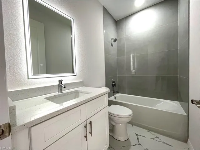 Bathroom with a textured wall, vanity, and  shower combination