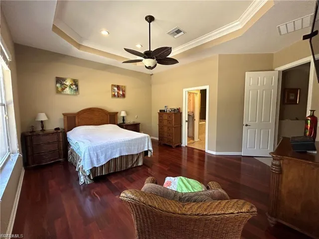 Spacious bedroom featuring rich wood-finish flooring, a tray ceiling with recessed lighting and a ceiling fan, and ample natural light from a large window