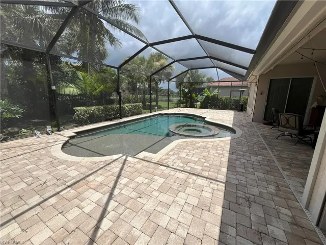 Screened outdoor area featuring a swimming pool with an integrated spa, extensive paver decking, and a covered patio section