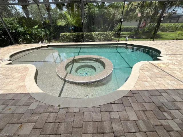 Freeform swimming pool featuring an integrated circular spa, sun shelf, and paver patio