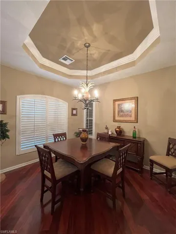 Tray ceiling with crown molding, wood-finish flooring, plantation shutters, and a central chandelier