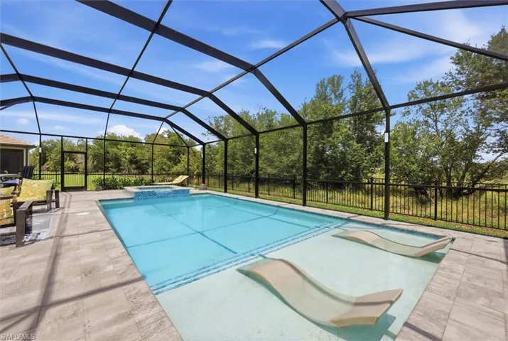 Expansive screened-in pool enclosure featuring a rectangular swimming pool with an integrated spa, sun shelf, and light-toned tile surround