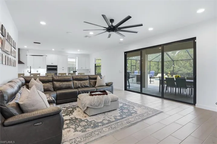 Open-concept living area with light-toned rectangular tile flooring, recessed lighting, and a black ceiling fan