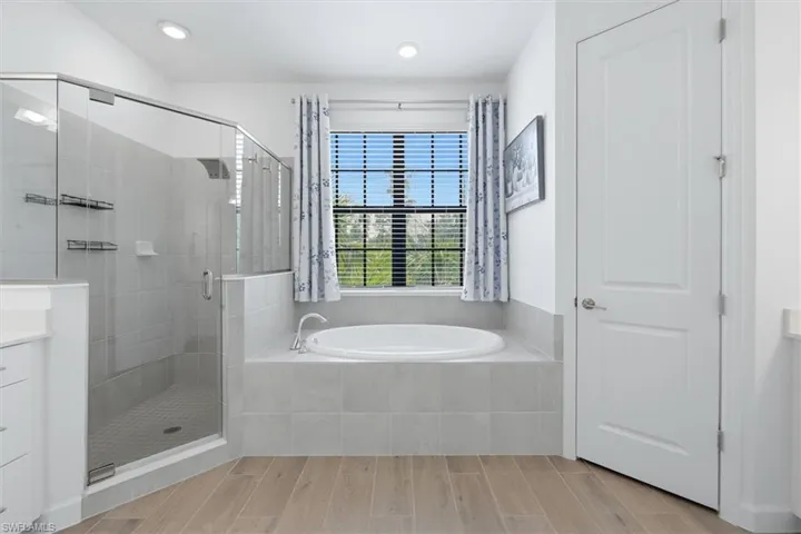 Bathroom featuring a glass-enclosed shower with tile surround, a built-in soaking tub with tile surround, and wood-finish flooring