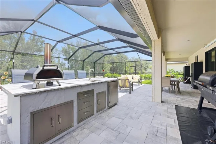 Screened outdoor living area featuring a built-in outdoor kitchen with integrated storage, a sink, and stone-finish countertops