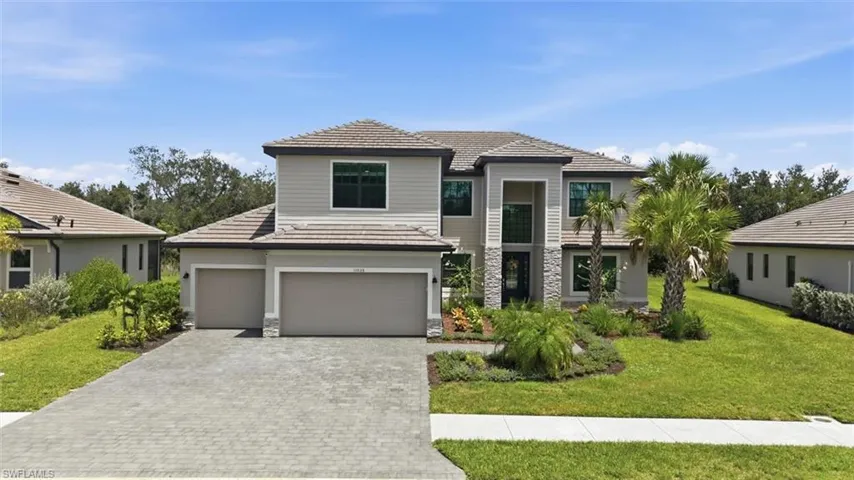 Contemporary two-story residence featuring a paver driveway, three-car garage, and a tiled roof