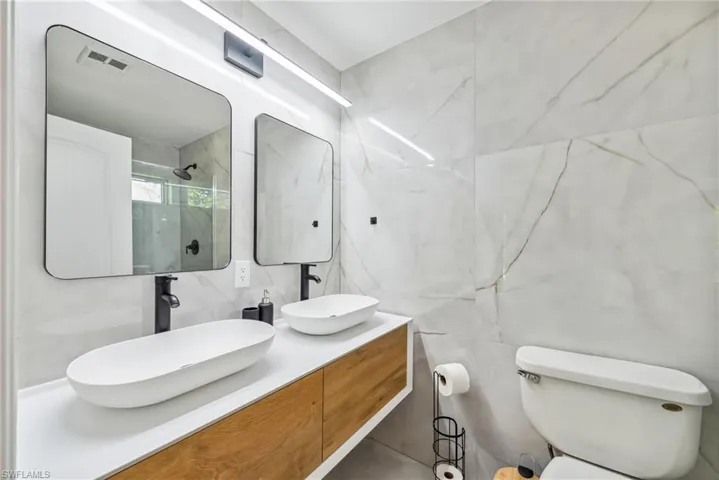 Bathroom with walk in shower, vanity, tile walls, and toilet