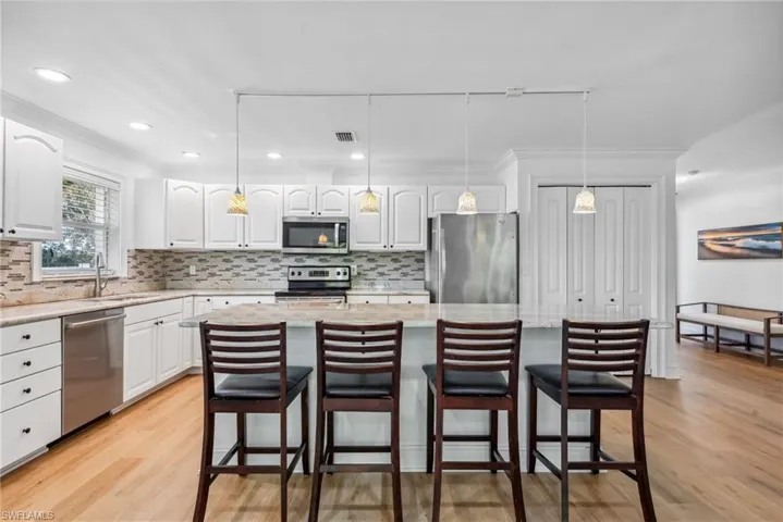Kitchen featuring stainless steel appliances, hanging light fixtures, white cabinetry, and a kitchen island