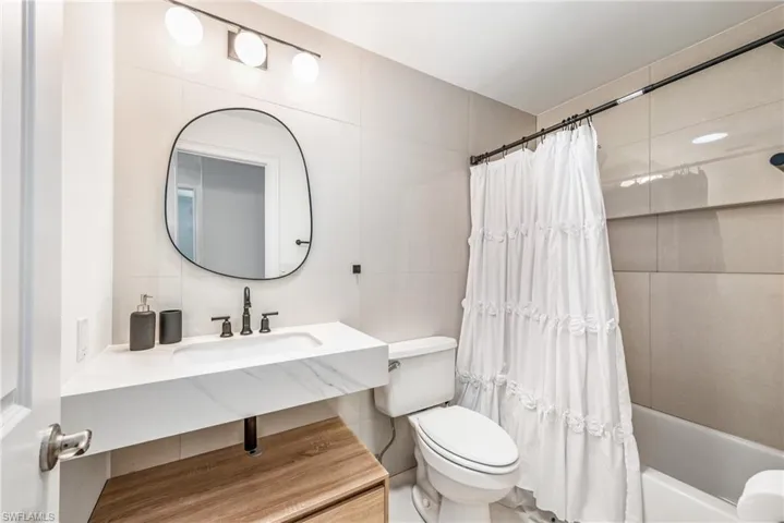 Full bathroom with tile walls, sink, backsplash, shower / bath combo with shower curtain, and toilet