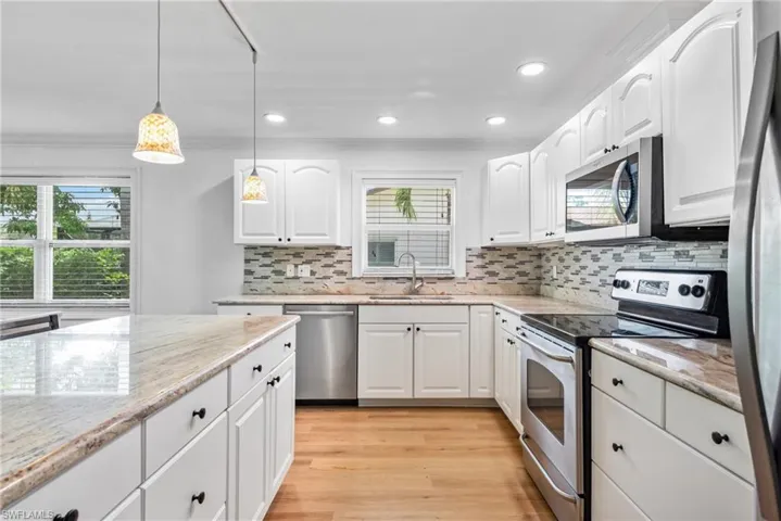 Kitchen with appliances with stainless steel finishes, hanging light fixtures, white cabinetry, and light hardwood / wood-style flooring