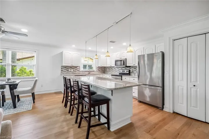 Kitchen featuring light hardwood / wood-style floors, a center island, a breakfast bar area, white cabinetry, and appliances with stainless steel finishes