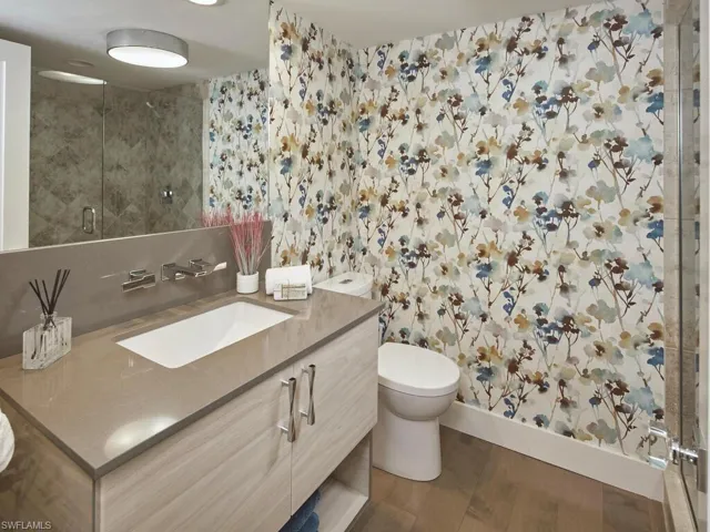 Bathroom with a stall shower, vanity, dark wood-style floors, and wallpapered walls