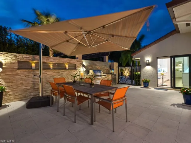 Patio at twilight with exterior kitchen, outdoor dining space, a patio area, and a gate