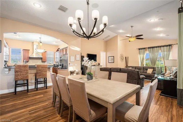 Dining area featuring dark wood-style floors, vaulted ceiling, a chandelier, arched walkways, and ceiling fan