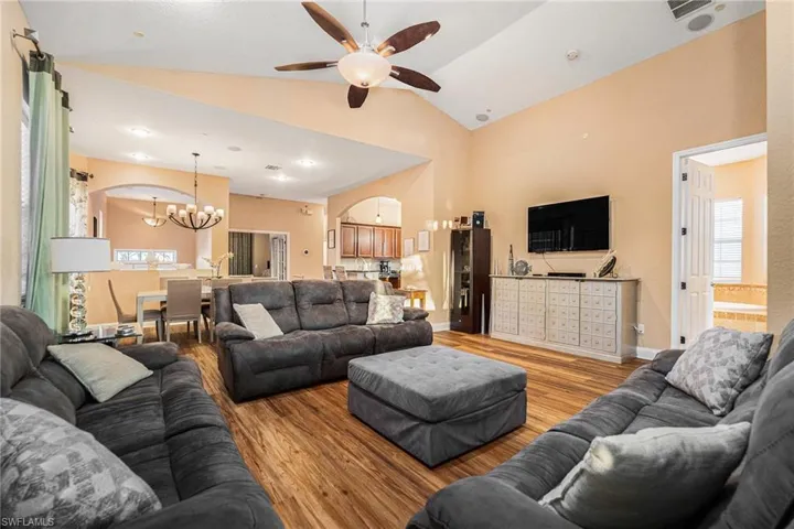 Living room featuring plenty of natural light, wood finished floors, vaulted ceiling, a ceiling fan, and a chandelier