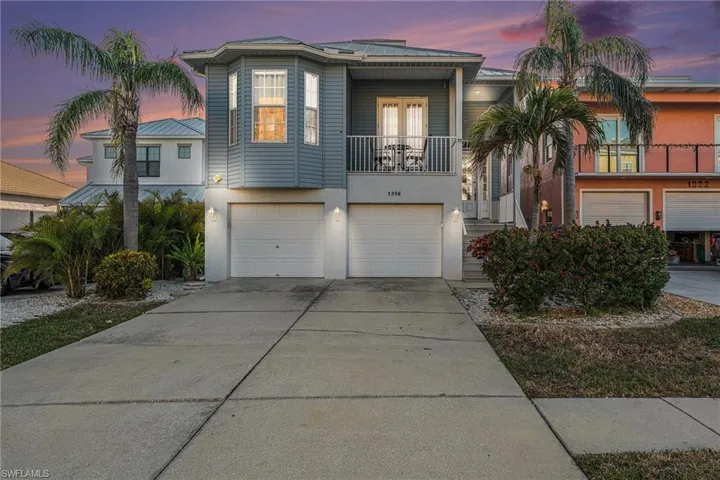 View of front of property with a balcony, driveway, a garage, french doors, and stucco siding