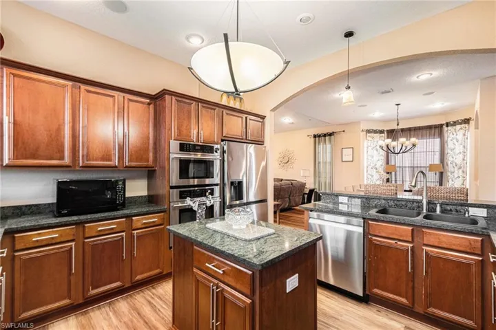 Kitchen featuring pendant lighting, arched walkways, appliances with stainless steel finishes, a chandelier, and a kitchen island