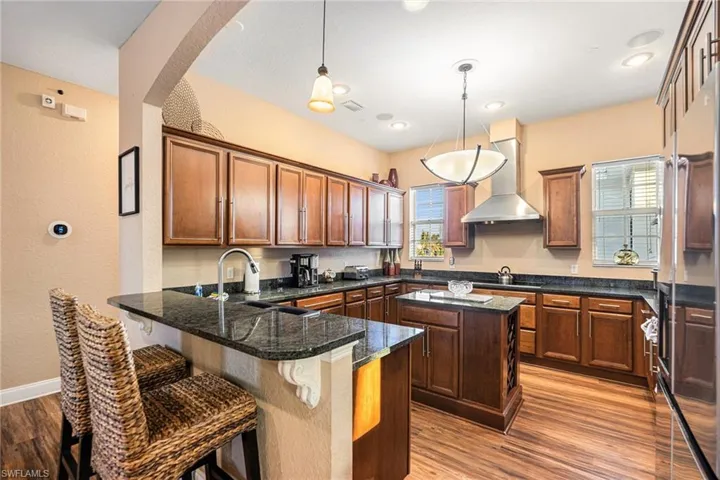 Kitchen with a breakfast bar area, a peninsula, pendant lighting, built in refrigerator, and light wood finished floors