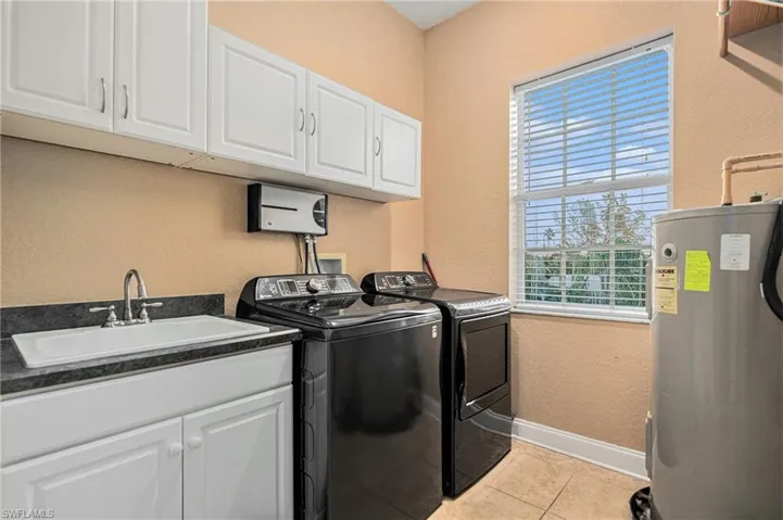 Laundry room on second floor featuring a textured wall, electric water heater, cabinet space, light tile patterned floors, and separate washer and dryer