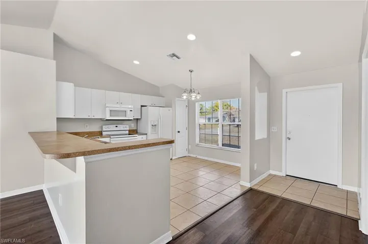 Kitchen with light wood-style floors, white appliances, suspended lighting, white cabinets, and a peninsula