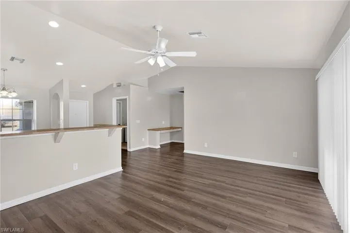 Unfurnished living room with lofted ceiling, dark wood-style flooring, ceiling fan, and hanging lights
