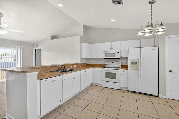 Kitchen featuring white appliances, suspended lighting, white cabinets, a peninsula, and ceiling fan
