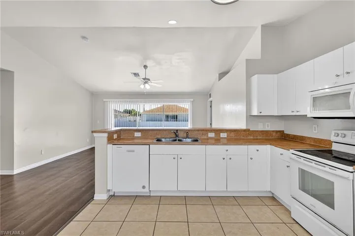 Kitchen featuring white appliances, vaulted ceiling, a peninsula, white cabinetry, and light tile patterned floors
