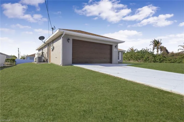 View of side of home with concrete driveway, stucco siding, a yard, and a garage