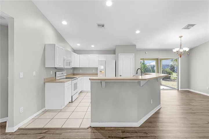 Kitchen featuring white appliances, light countertops, light wood-style flooring, white cabinets, and a kitchen breakfast bar