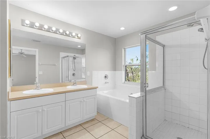Full bath with double vanity, light tile patterned flooring, a stall shower, a bath, and recessed lighting