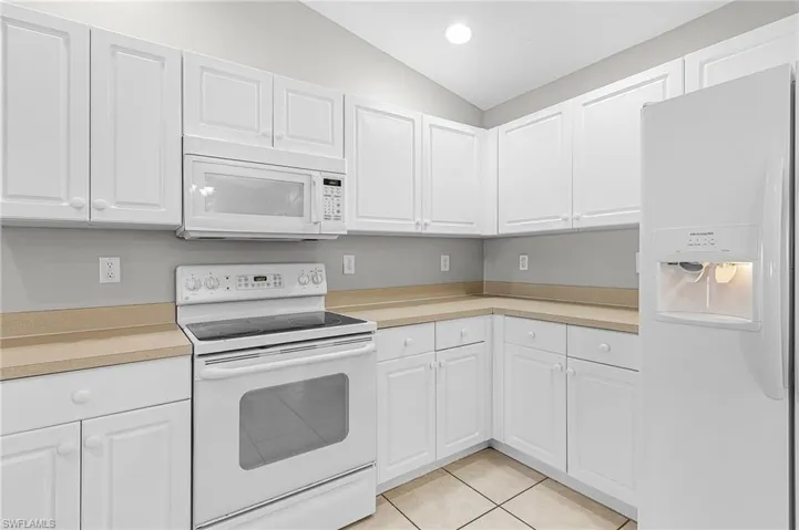 Kitchen with white appliances, light countertops, white cabinets, vaulted ceiling, and light tile patterned floors