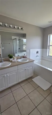 Full bath featuring a bath, double vanity, light tile patterned floors, and a shower stall