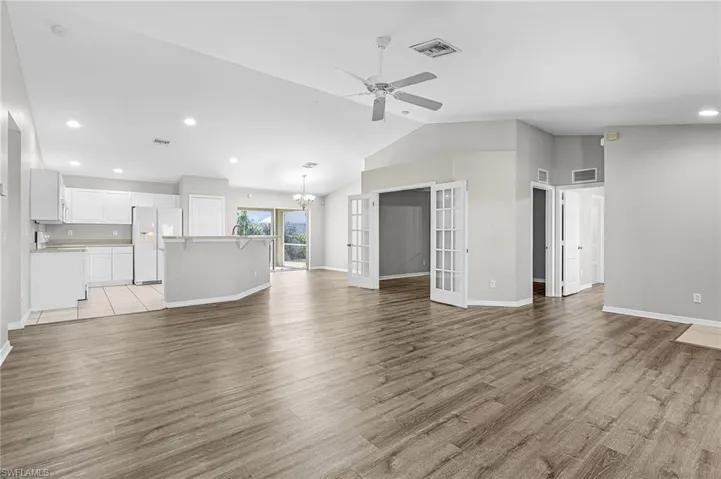 Unfurnished living room with lofted ceiling, recessed lighting, french doors, a chandelier, and light wood-style floors