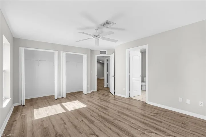 Unfurnished bedroom featuring two closets, light wood finished floors, ceiling fan, and ensuite bath