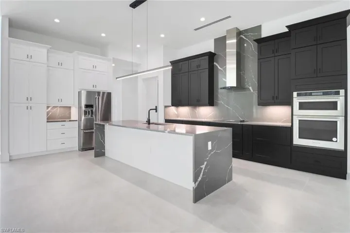 Kitchen with white cabinetry, wall chimney exhaust hood, stainless steel appliances, tasteful backsplash, and a center island with sink