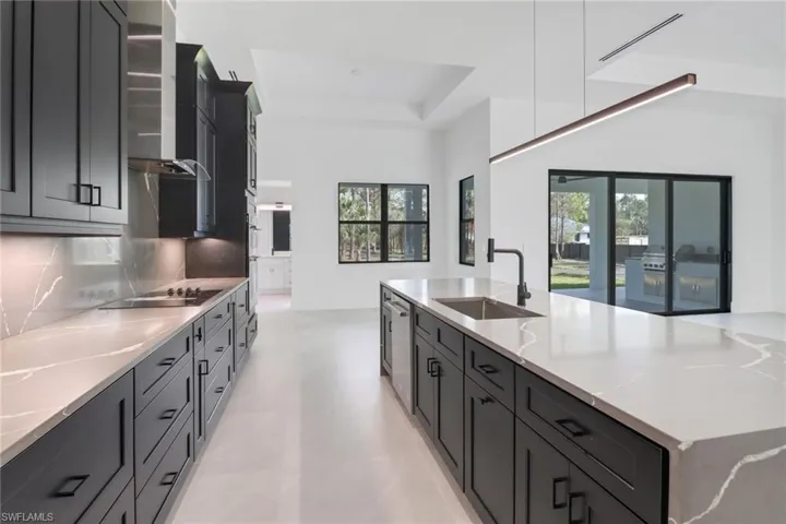 Kitchen with black electric stovetop, light stone counters, a tray ceiling, wall chimney range hood, and sink