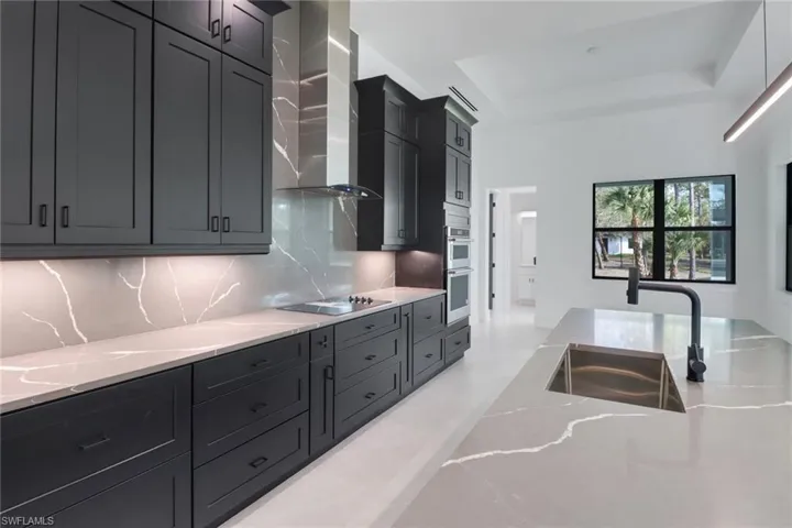 Kitchen featuring black electric stovetop, wall chimney range hood, sink, a tray ceiling, and tasteful backsplash