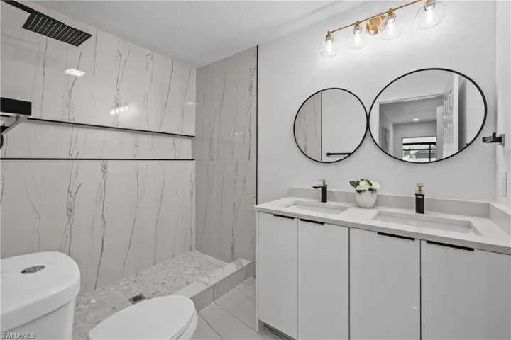 Bathroom featuring double vanity, toilet, a tile shower, tile flooring, and a textured ceiling