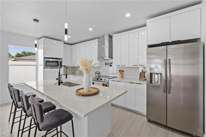Kitchen featuring light hardwood / wood-style floors, hanging light fixtures, white cabinetry, appliances with stainless steel finishes, and wall chimney exhaust hood