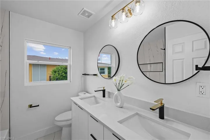 Bathroom with double vanity, tile flooring, and toilet