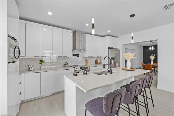 Kitchen featuring decorative light fixtures, appliances with stainless steel finishes, sink, and wall chimney exhaust hood