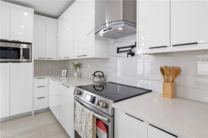 Kitchen featuring light hardwood / wood-style flooring, backsplash, electric range, wall chimney exhaust hood, and white cabinets