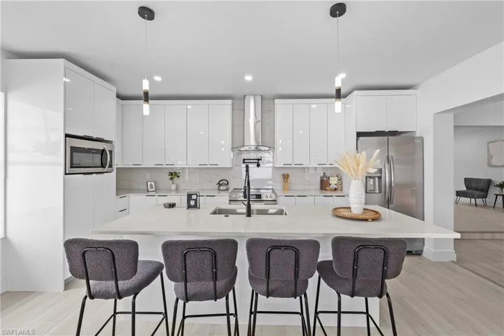Kitchen featuring appliances with stainless steel finishes, white cabinetry, pendant lighting, and wall chimney exhaust hood